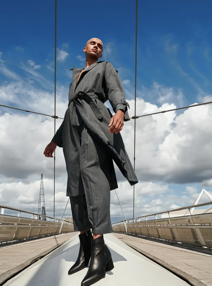 Person in a long coat standing on a bridge under clouds