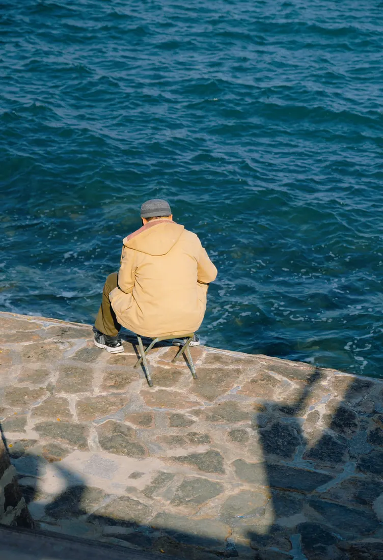 Person sitting at the end of a stone pier by the sea